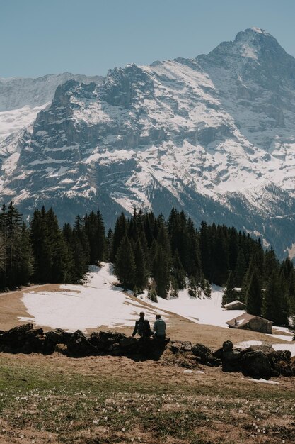 Two people sitting on a stone wall in front of a snowy mountain