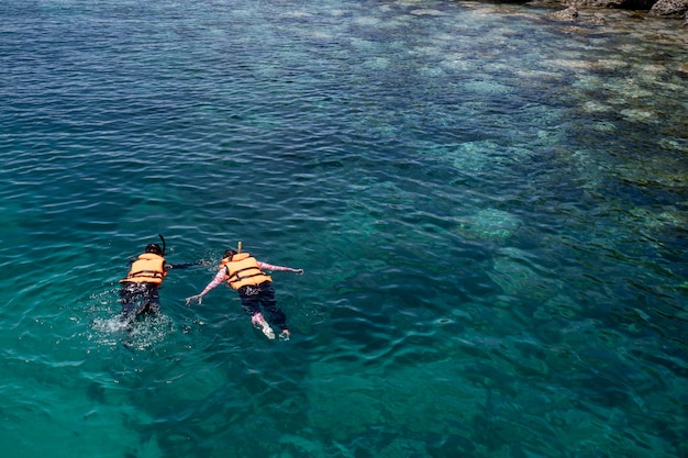 Two people snorkeling wear a life jacket over coral reef with clear blue ocean water in tropical clear sea