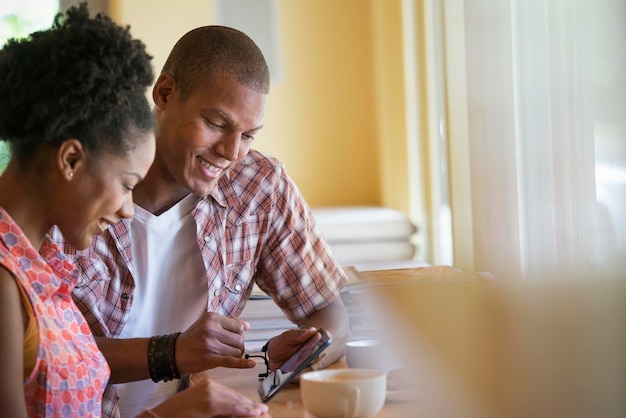 Two people using a digital tablet seated close together at a cafe Coffee cups