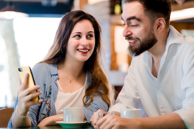 Two people using a mobile phone together while drinking a cup of coffee at a coffee shop.