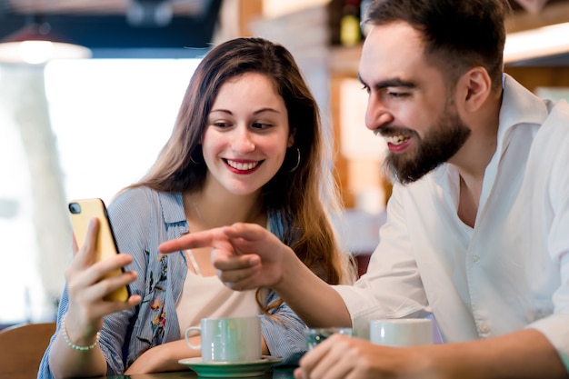 Two people using a mobile phone together while drinking a cup of coffee at a coffee shop.