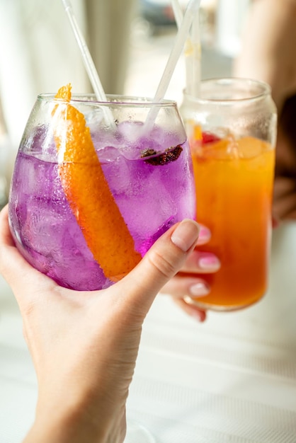 Two person cheers with glasses filled with refreshing summer cocktails in hands