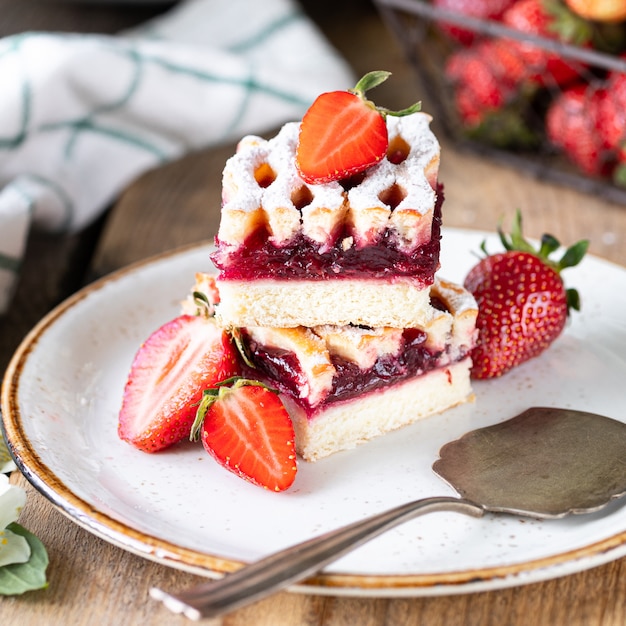 Two piece of strawberry pie on a plate on wooden table. Square