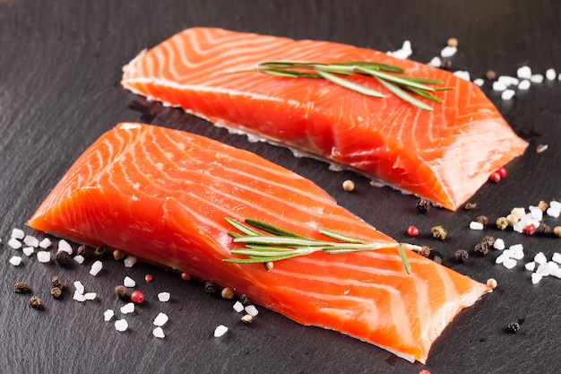 Two pieces of fresh salmon fillet with spices on a black slate surface