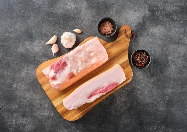 Two pieces of raw pork lard with spices on wooden board top view