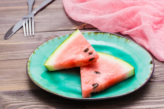 Photo two pieces of watermelon on a ceramic plate, cutlery and napkin on a wooden background