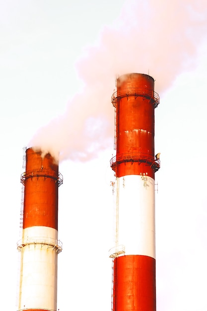 Two pipes and smoke. Close-up from below of smoke coming out of pipes against blue sky. Two chimneys with thick white smoke. Concept air pollution, environmental problems, air emissions. Copy space