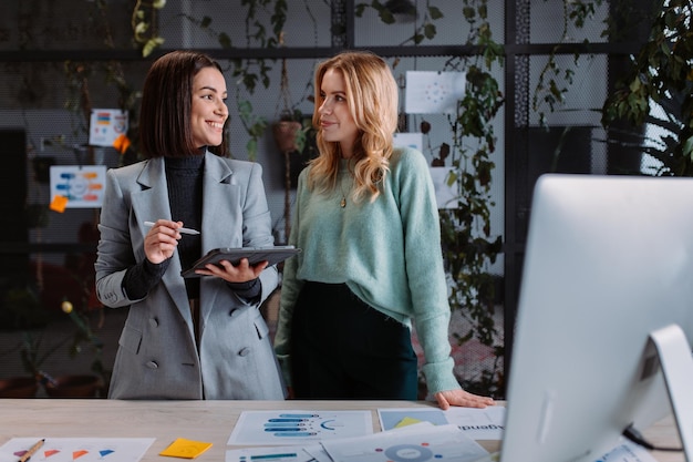 Two positive female colleagues looking at each other and discussing something at the office women