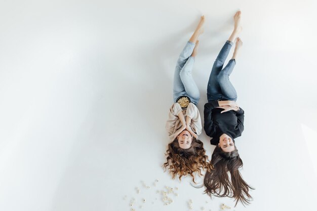 Two pretty cheerful young girls friends standing isolated over white background, eating popcorn