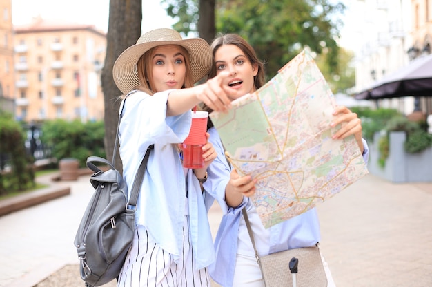 Two pretty girls dressed in summer clothes holding city map while standing outdoors.