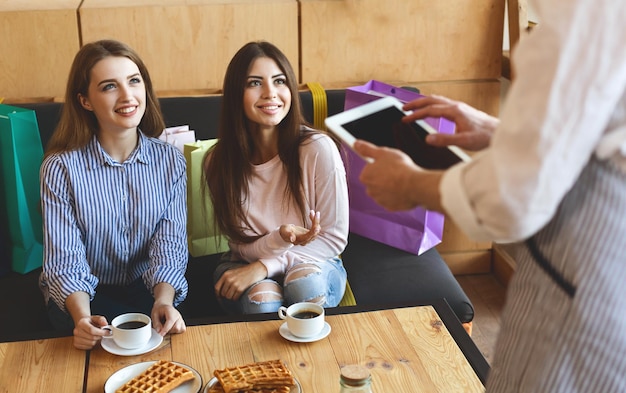 Two pretty girls flirting with waiter in cafe, digital tablet with black blank screen