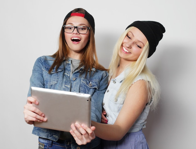 Two pretty hipster girls taking a self portrait with a tablet, over white background, not isolated