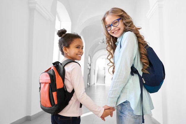 Two pretty school girls blonde Caucasian and brunette African holding each other by hands and smiling