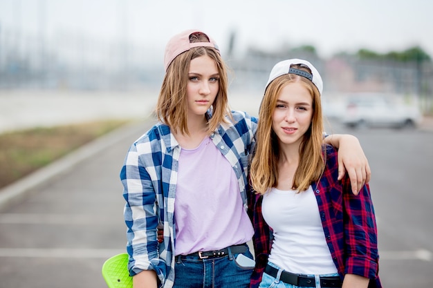 two pretty smiling blond girls wearing checkered shirts, caps and denim shorts 