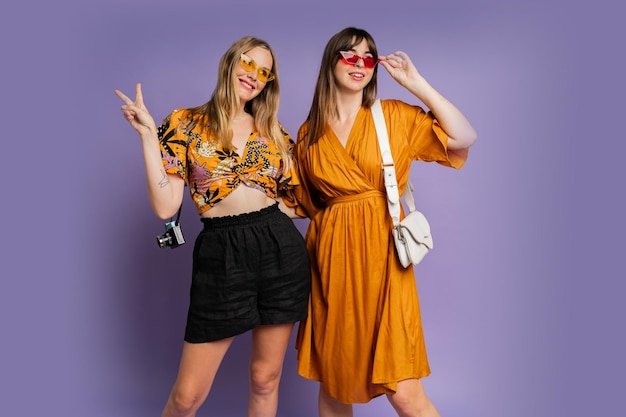 Two pretty women best friends posing on purple background in trendy summer outfit