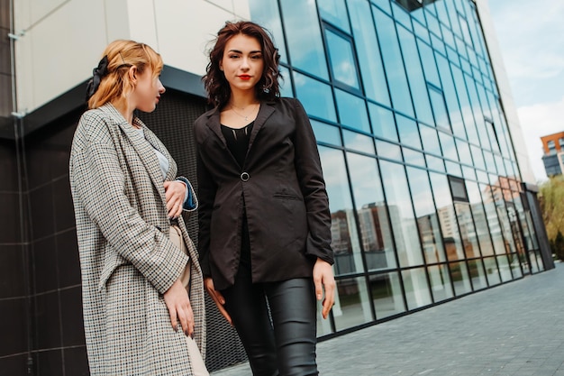 Two pretty women friends posing near glass building. Couple of gay lesbian girls hugging embracing