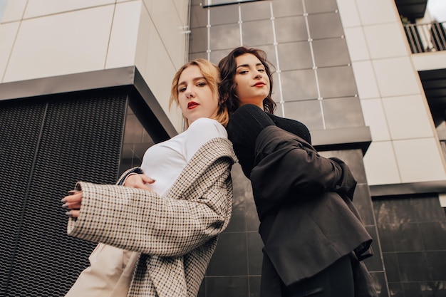 Two pretty women friends posing near glass building. Couple of gay lesbian girls hugging embracing