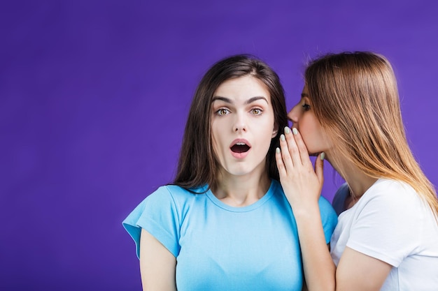 Two pretty women gossipping with face reaction expression before blue background