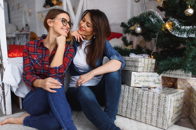 Two pretty young girls or women are sitting near a New Year or Christmas tree.