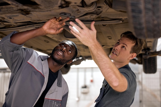 Two professional auto mechanics working on undercarriage of car diligence attention inspection exami