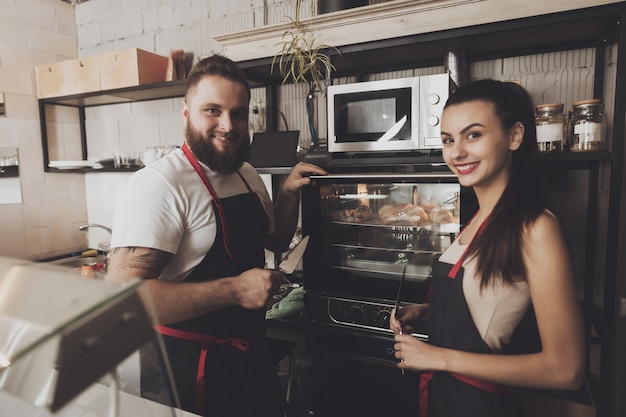 Two professional bakers are standing near oven.