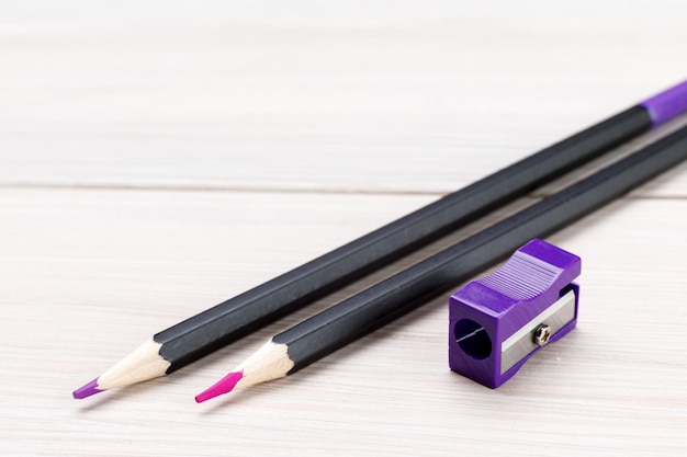 Two professional colored pencils and a purple pencil sharpener on a light wooden table. Sharpened purple and pink pencils close-up