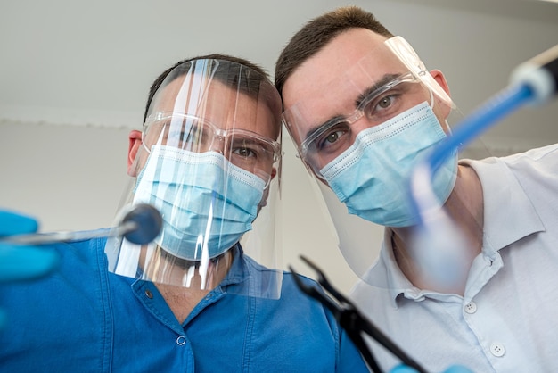 Two professional confident dentists posing near a dental chair in a clinic