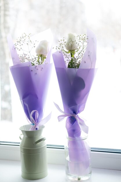 Two purple flowers are on a window sill with a white flower in the middle.