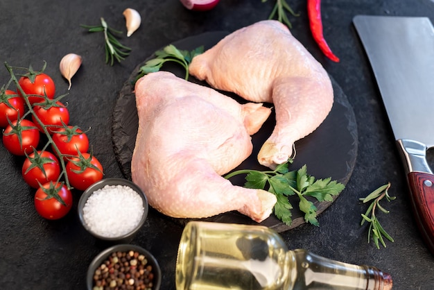 two raw chicken legs with spices and herbs on a stone background