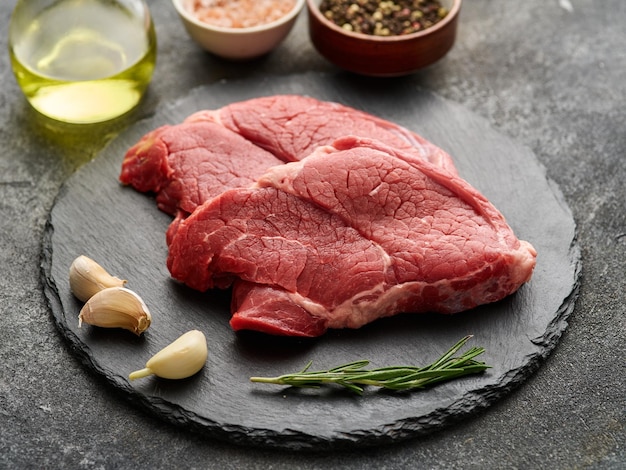 Two Raw Entrecote with garlic rosemary pepper and salt on a black board closeup