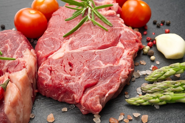 Two raw marbled beef steaks with spices and vegetables