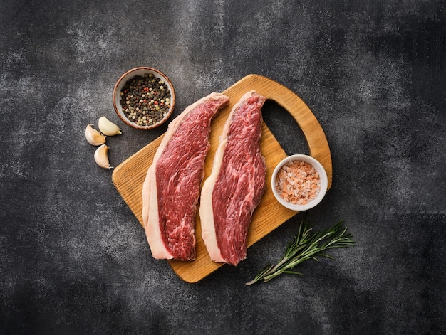 Two Raw Picanha steak on wooden board in rustic style with salt garlic and pepper Copyspace Top view