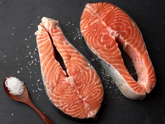 Two raw salmon steaks with white salt on a black background