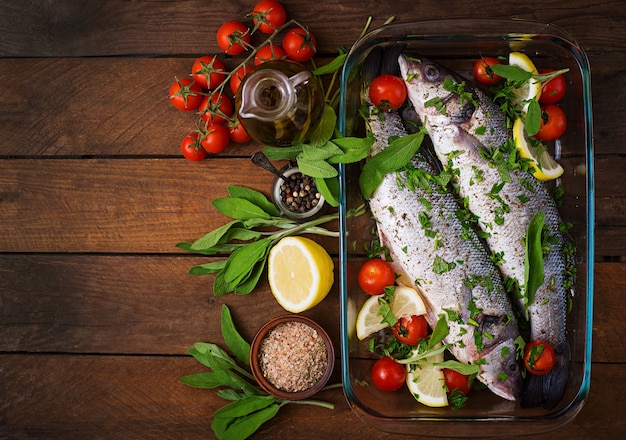 Two raw seabass in a baking dish with spices on an old wooden background. Top view