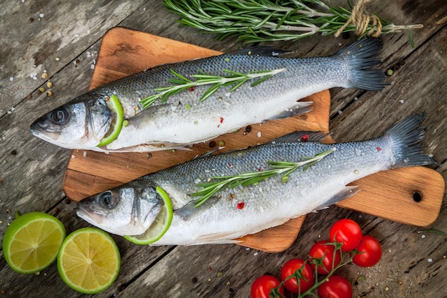 Two raw seabass with lime cherry tomatoes and rosemary on the wooden background