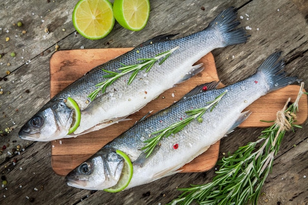 Two raw seabass with lime and rosemary on the wooden background