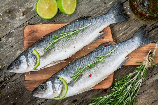 Two raw seabass with lime and rosemary on the wooden background