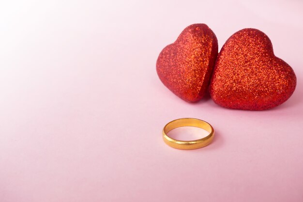 Two red heart objects with golden ring on pink background. Symbolic of valentine and love 