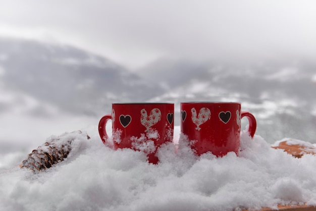 Two red mugs with heart shaped on the snow and mountain background valentine concept