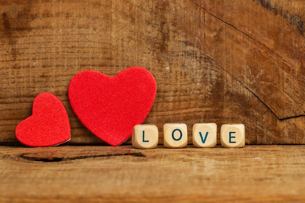 Two red paper hearts on a wooden background with a love sign