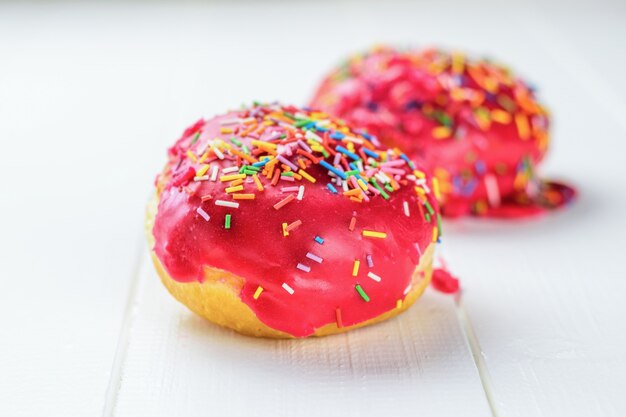 Two red pastries in colorful topping on a white wooden table