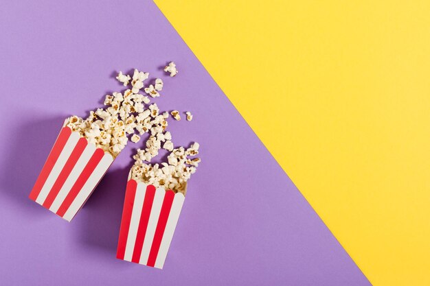 Two red striped paper buckets with popcorn top view on color background