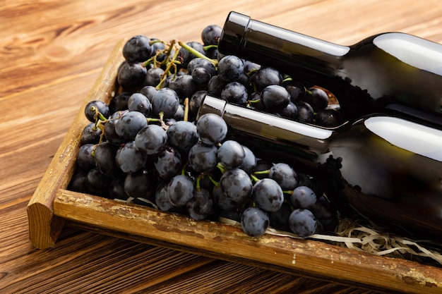 Two Red Wine bottles composition on brown wooden table. Red wine bottles in box on black ripe grapes on wooden table. Old collection wine.