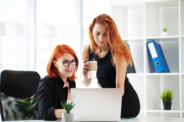 Two redhaired businesswomen in a coworking space with a laptop on the desktop in the office