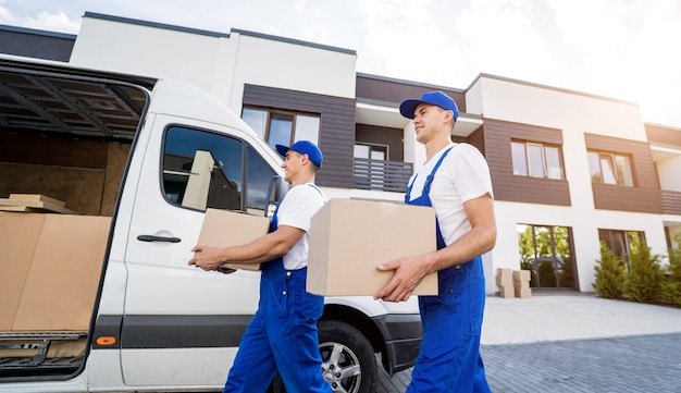 Two removal company workers are loading boxes and furniture into a minibus