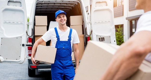 Two removal company workers unloading boxes from minibus into customers home