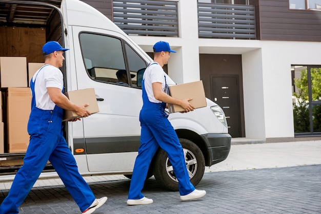 Two removal company workers unloading boxes from minibus into new home