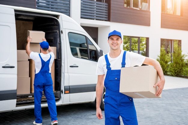 Two removal company workers unloading boxes from minibus into new home