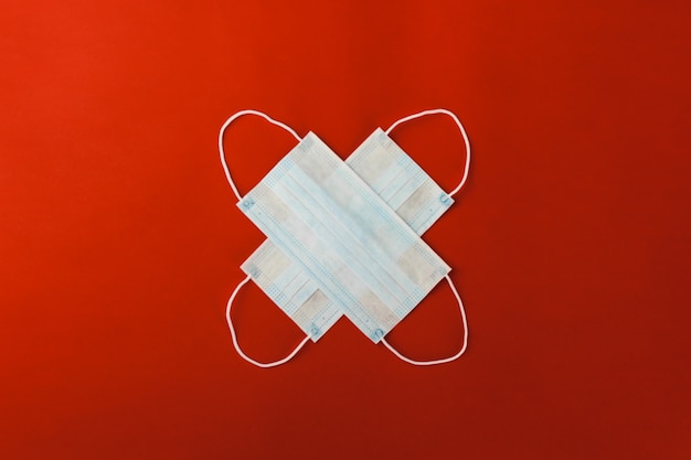 Two respiratory medical protective masks lie in the shape of a cross on a red background.