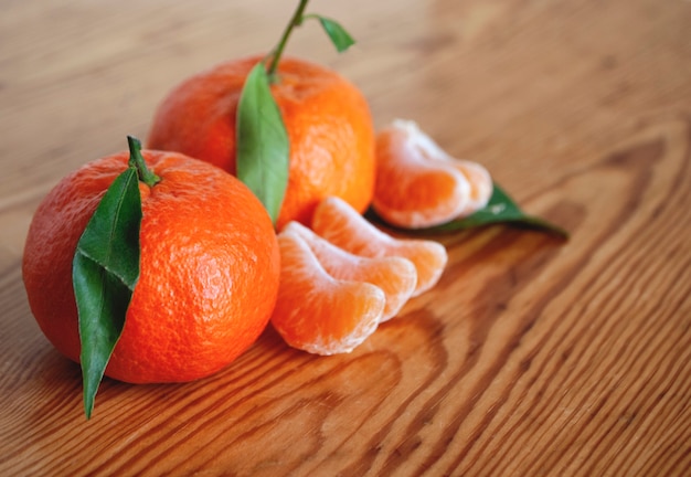 Two ripe tangerines next to slices of peeled tangerines on a wooden table